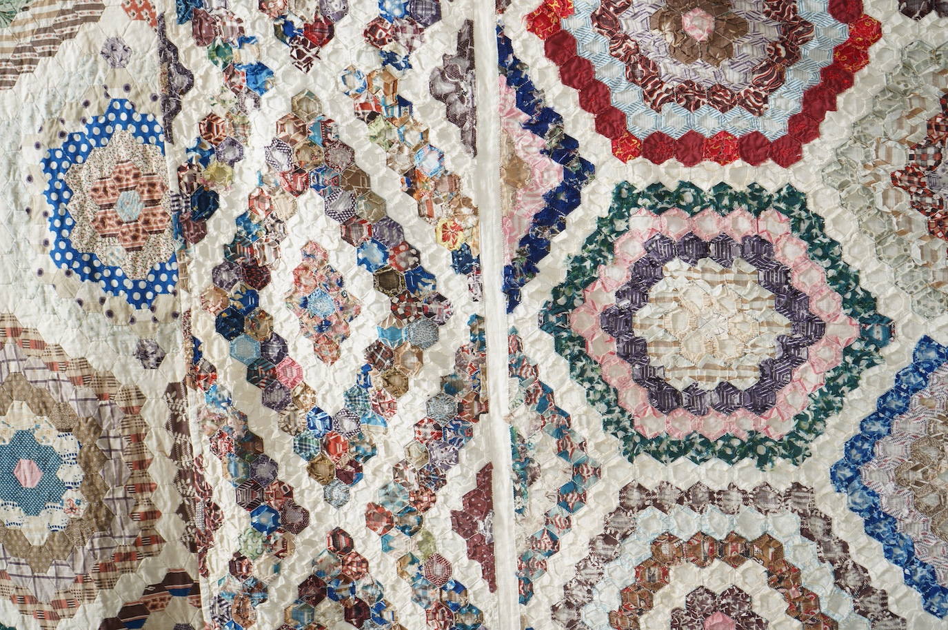 A large 19th century ‘Grandmother’s Flower Garden’ cotton patchwork bedspread, using dress fabric scraps from the day to create hexagonal concentric patterns which form a flower like shape/pattern, 282 x 254cm. Condition